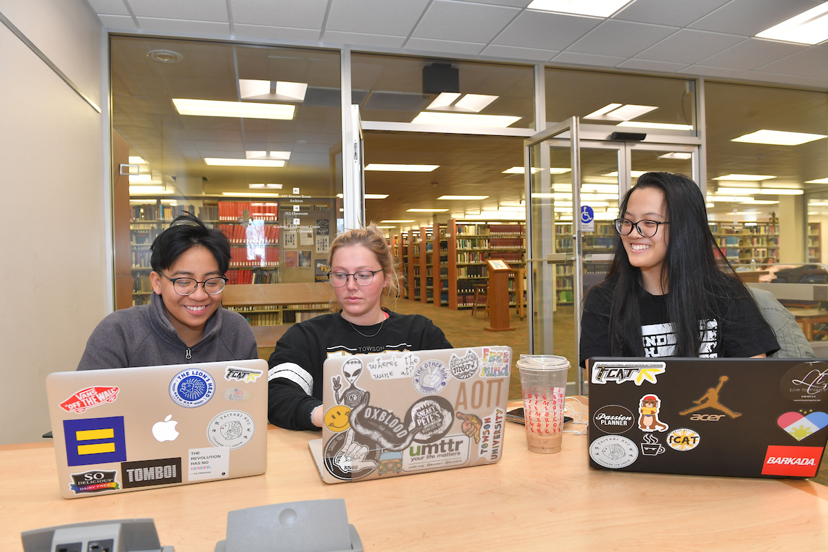 three students with laptops smiling